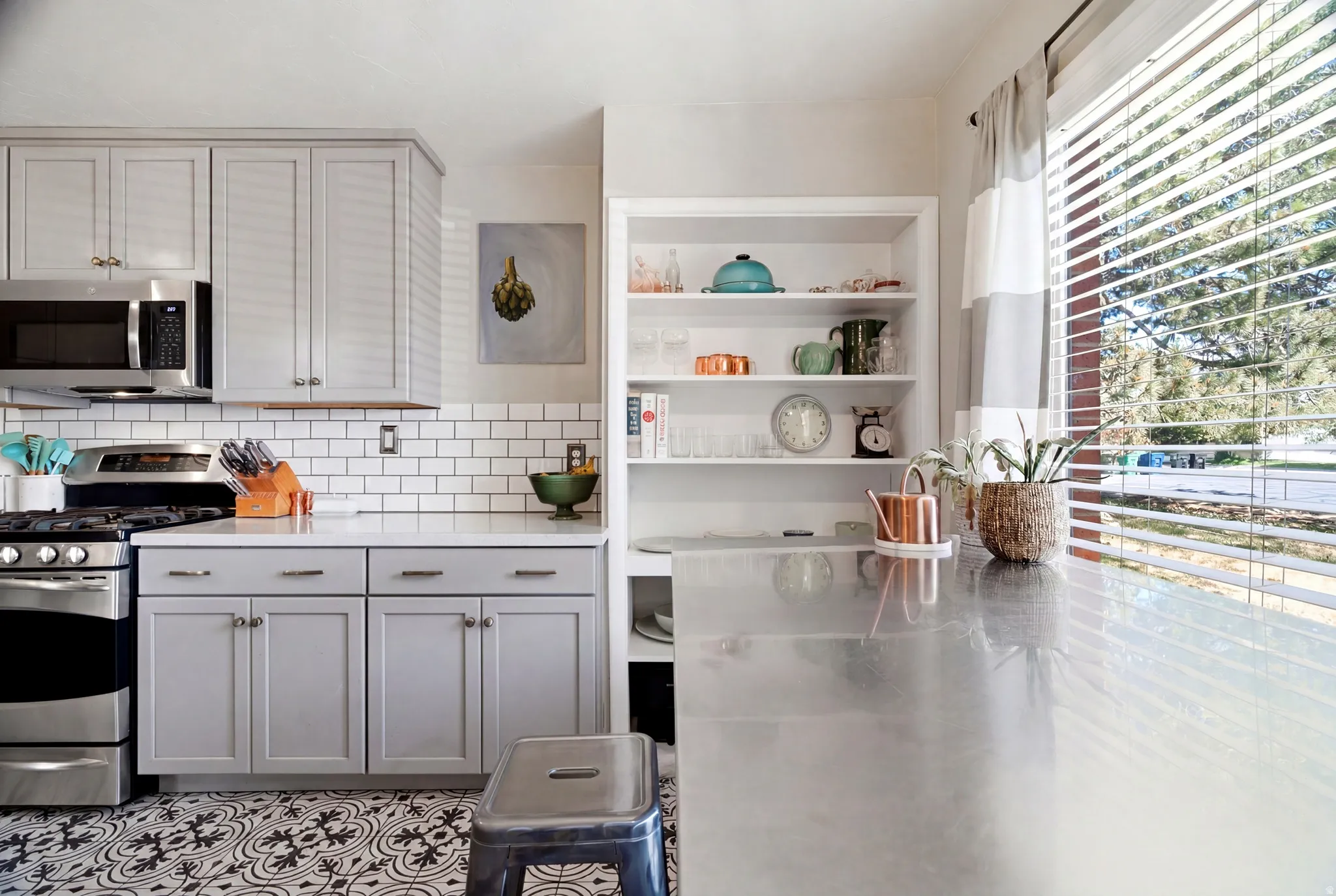 Well-appointed kitchen featuring light gray cabinetry, stainless steel appliances, a white subway tile backsplash, and patterned floor tiling