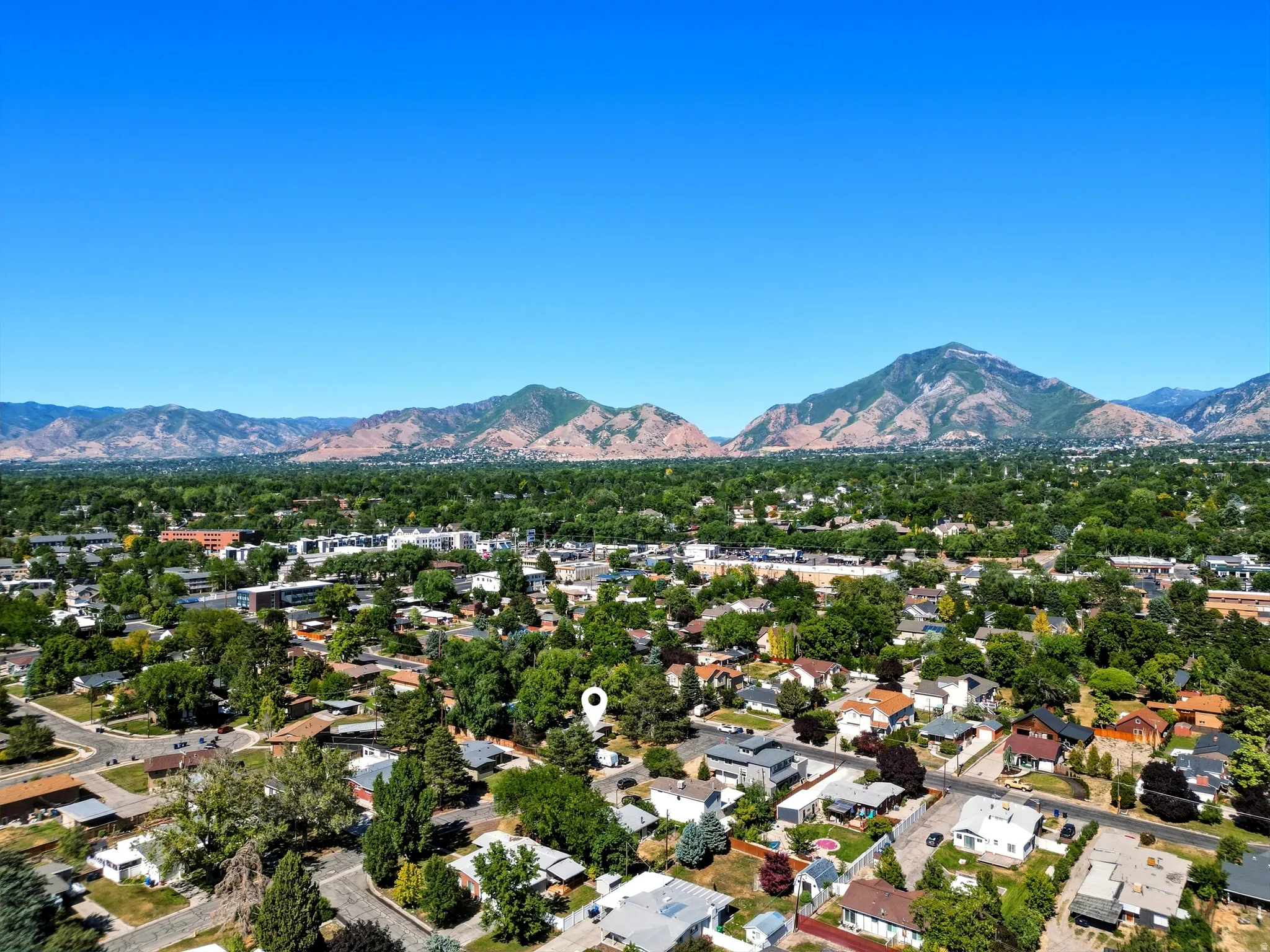 Expansive aerial perspective showcasing a residential area with varied architectural styles, abundant mature trees, and mountainous terrain in the background