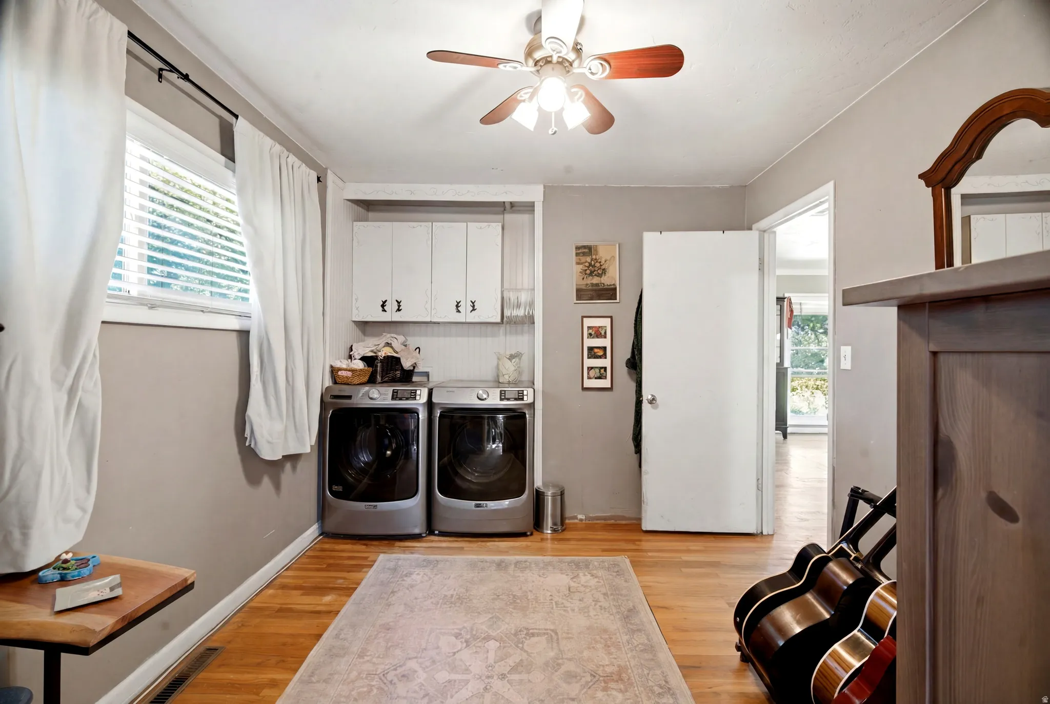 Dedicated laundry area featuring a window, hardwood-finish flooring, overhead cabinetry, a ceiling fan, and beadboard paneling