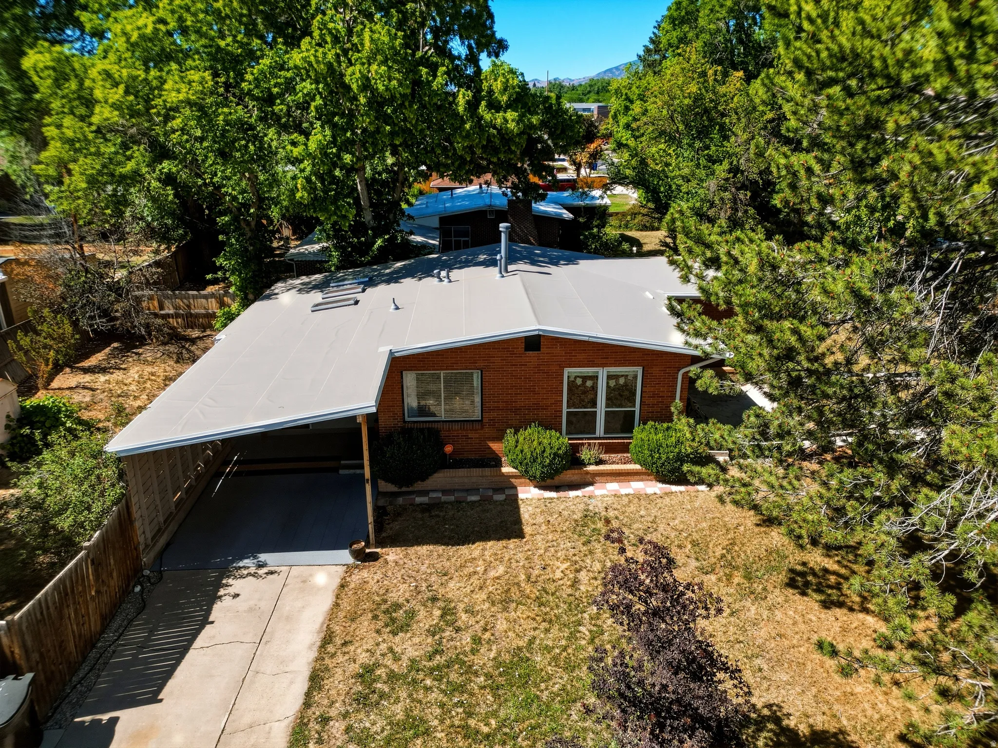Brick exterior residence featuring a carport, mature perimeter trees, and a front yard with established shrubs