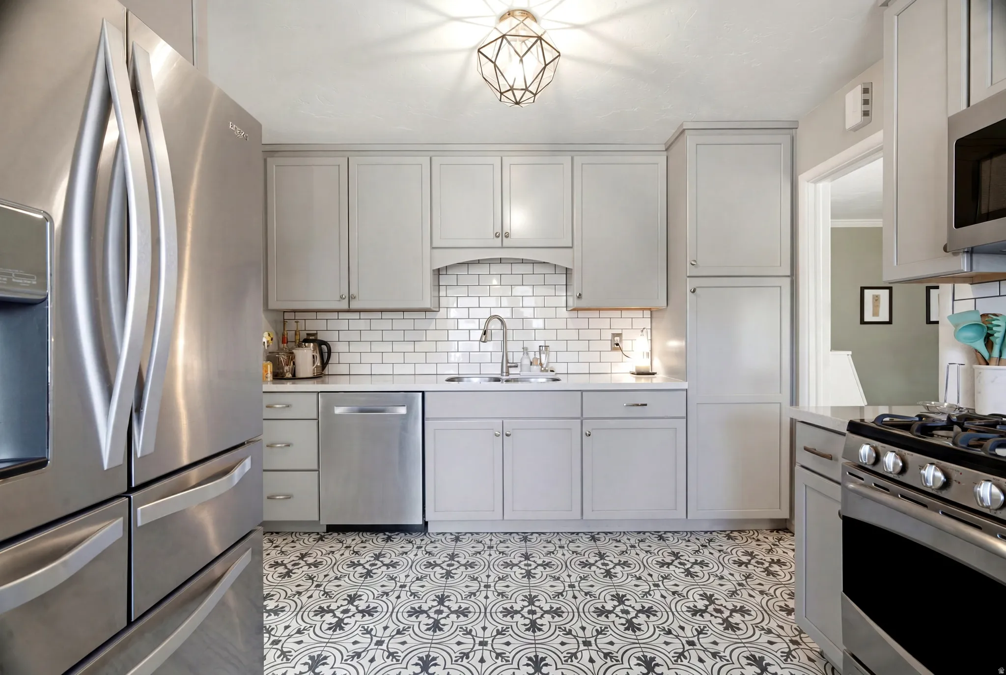 Kitchen featuring light gray cabinetry, subway tile backsplash, patterned floor tiling, stainless steel appliances, and a recessed sink