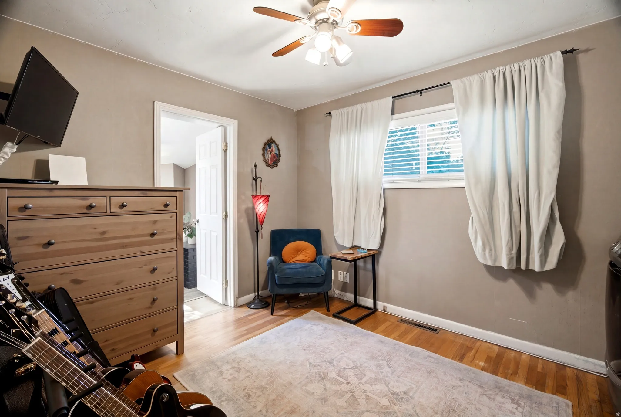 Room featuring wood-finish flooring, a ceiling fan with light fixture, and a window with blinds and drapes