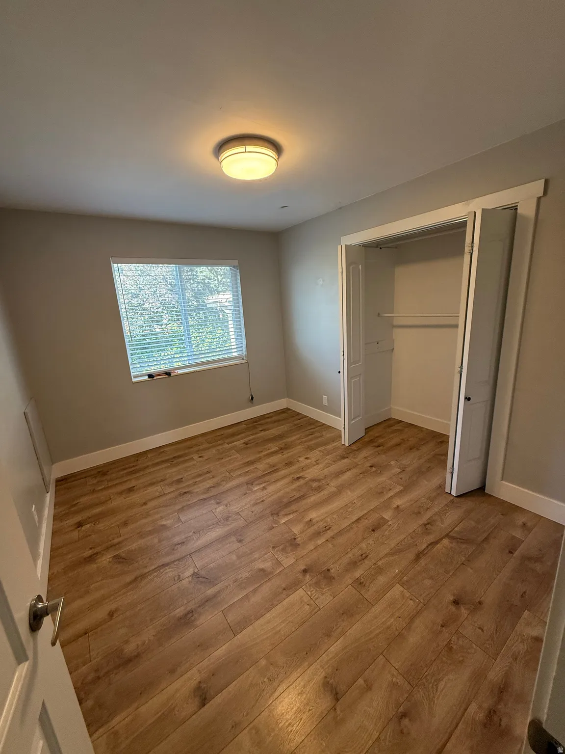 Wood-finish flooring, flush mount ceiling light, window with blinds, and bi-fold closet doors