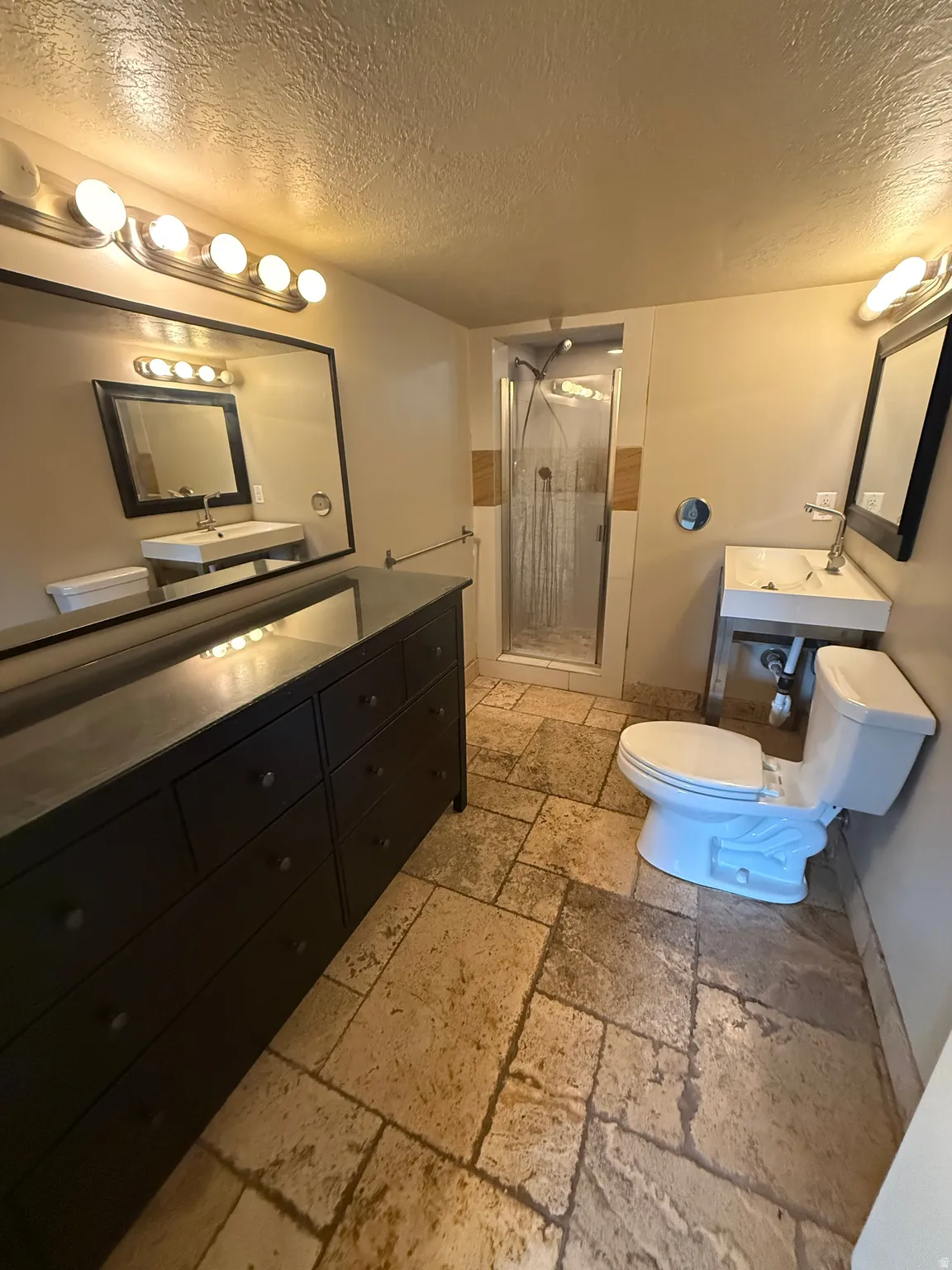 Stone tile flooring, dual vanities with integrated sinks, and a glass-enclosed shower