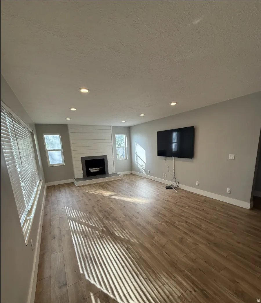 Spacious room featuring wood-finish flooring, recessed lighting, and multiple windows with blinds