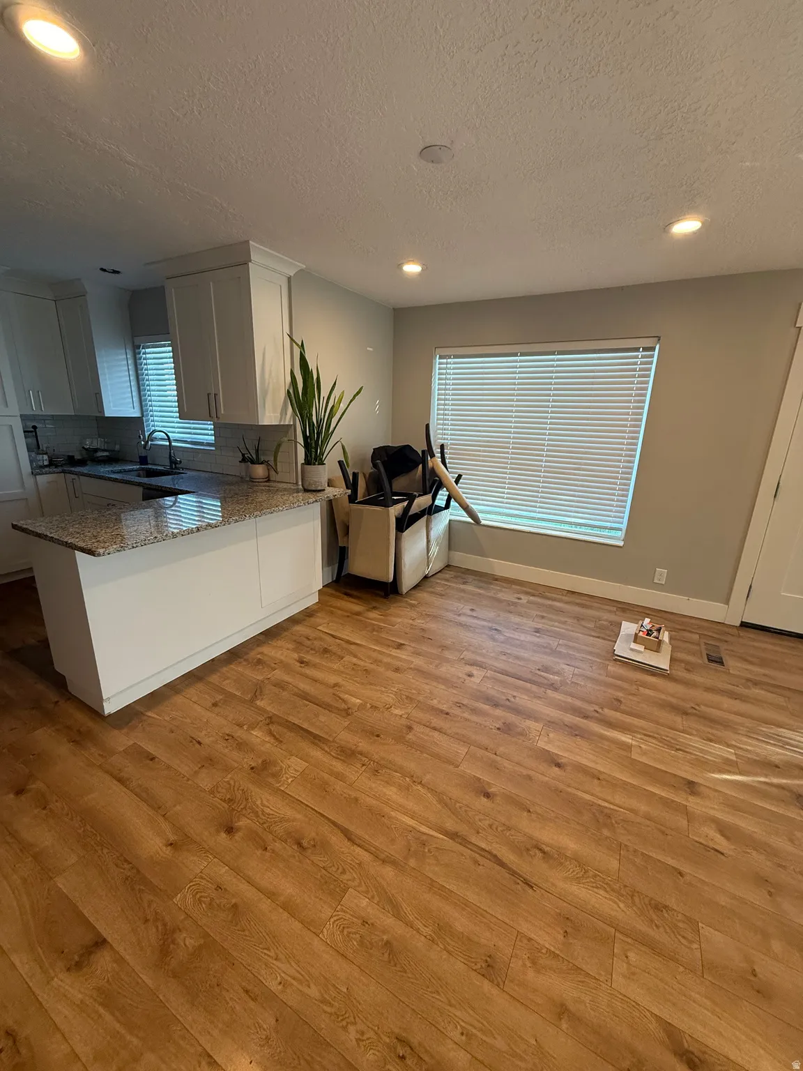 Wood-finish flooring, recessed lighting, white cabinetry, a kitchen island with a stone-finish countertop, and a window with horizontal blinds