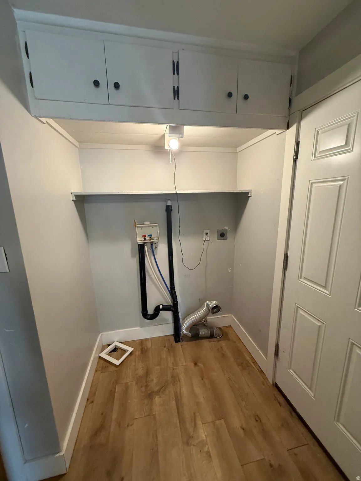 Built-in upper cabinetry, utility shelf, and wood-finish flooring