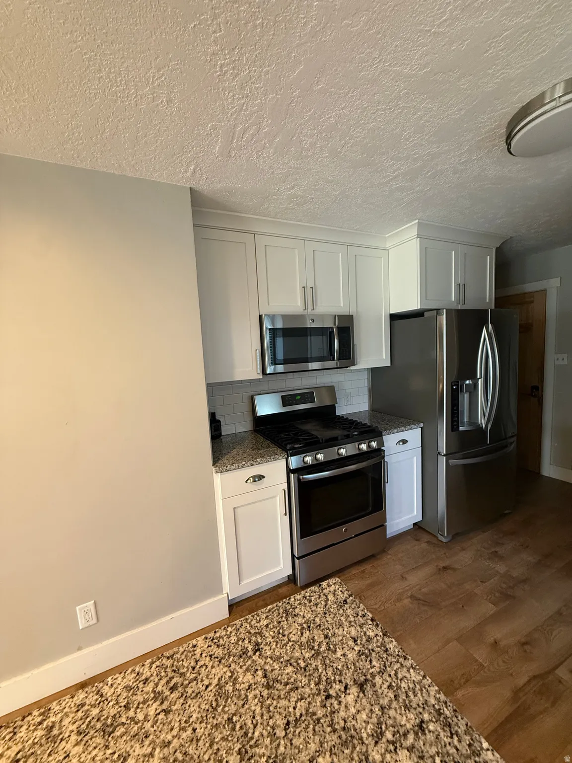 Kitchen featuring white shaker cabinetry, stainless steel appliances, speckled countertops, and a subway tile backsplash
