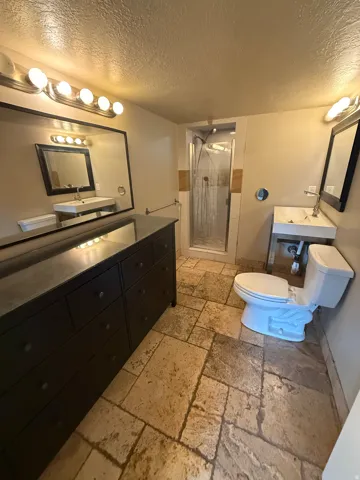 Stone tile flooring, dual vanities with integrated sinks, and a glass-enclosed shower