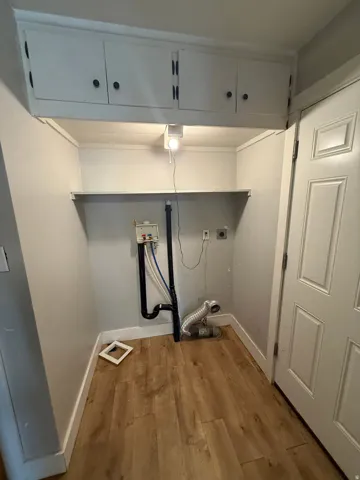 Built-in upper cabinetry, utility shelf, and wood-finish flooring