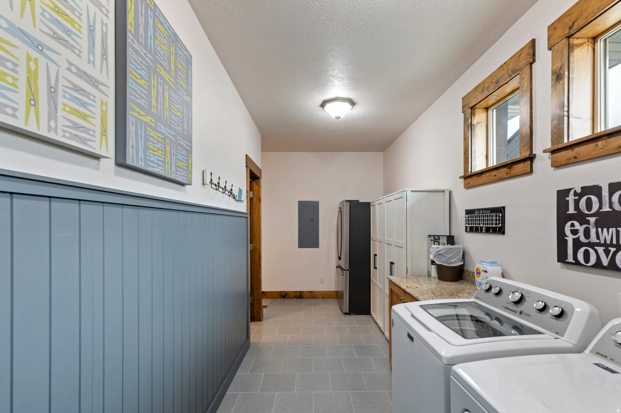 Utility room featuring a washer and dryer set, granite-look countertop, wood-paneled wainscoting, and tile flooring