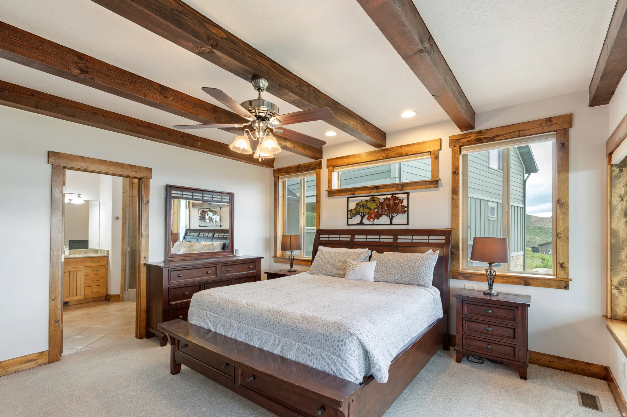 Spacious bedroom featuring exposed wood ceiling beams, white walls, and light-toned carpet flooring