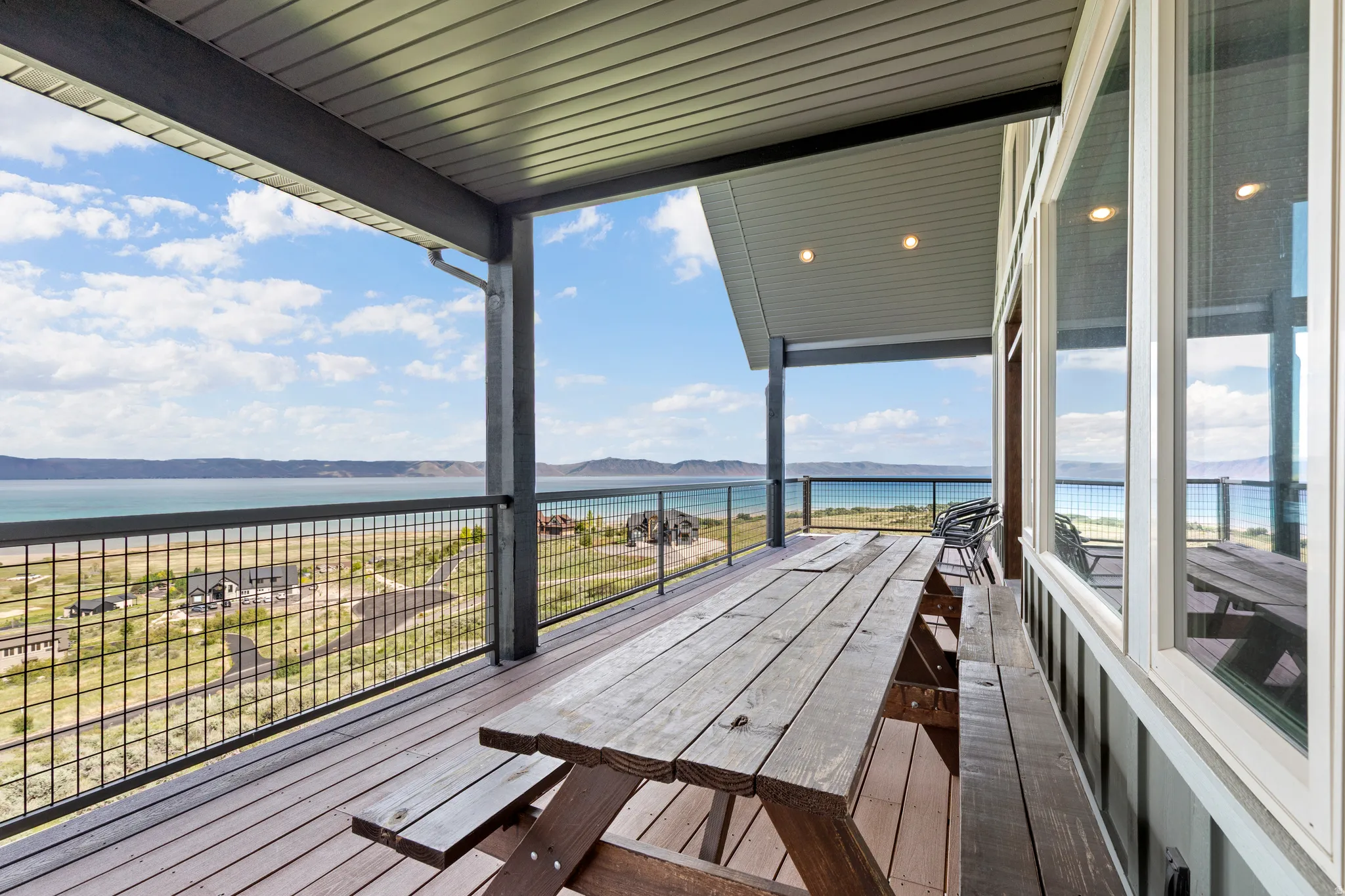 Expansive covered deck featuring composite decking, recessed lighting, white framed windows, and metal grid railing
