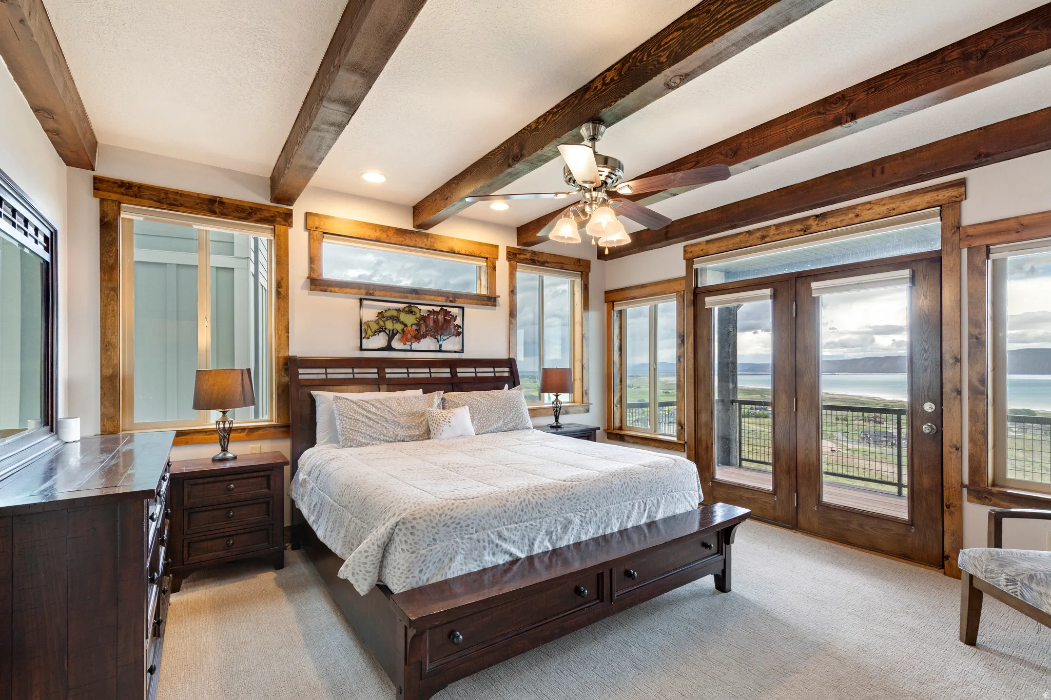 Spacious room featuring wood-finish ceiling beams, wood-trimmed windows, and a French door balcony access