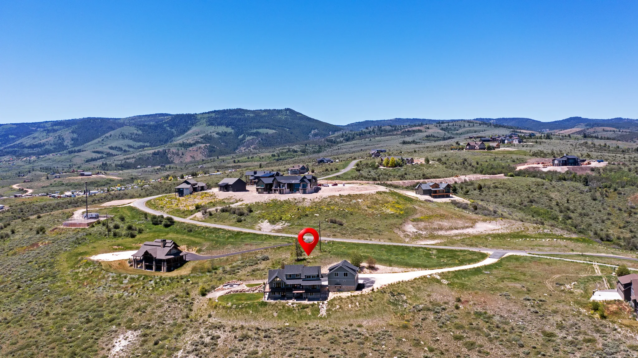 Expansive mountain landscape featuring a large residential property, paved access roads, and multiple structures