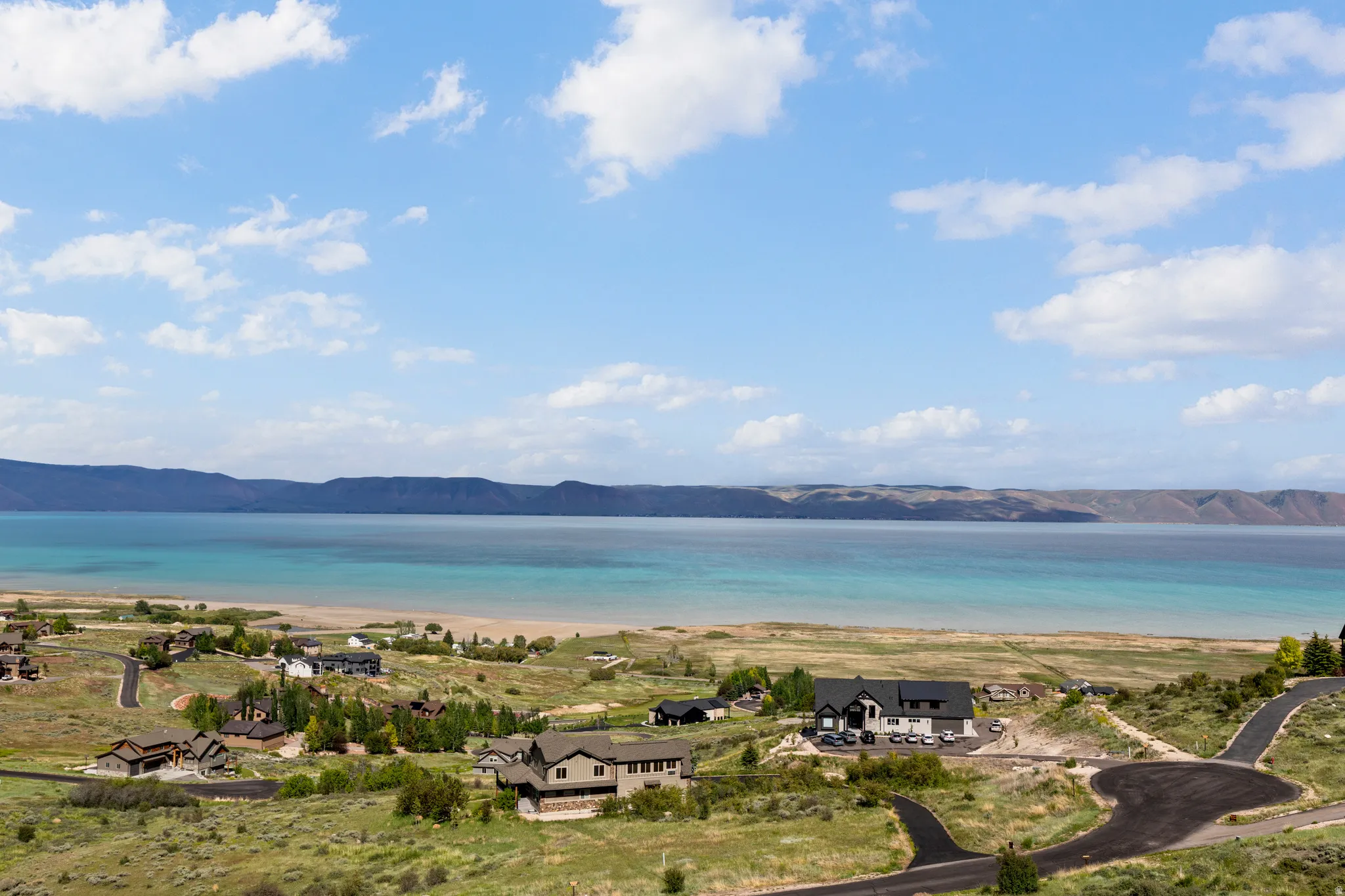 Expansive lakefront property featuring a sandy beach, clear blue water, and distant mountain ranges