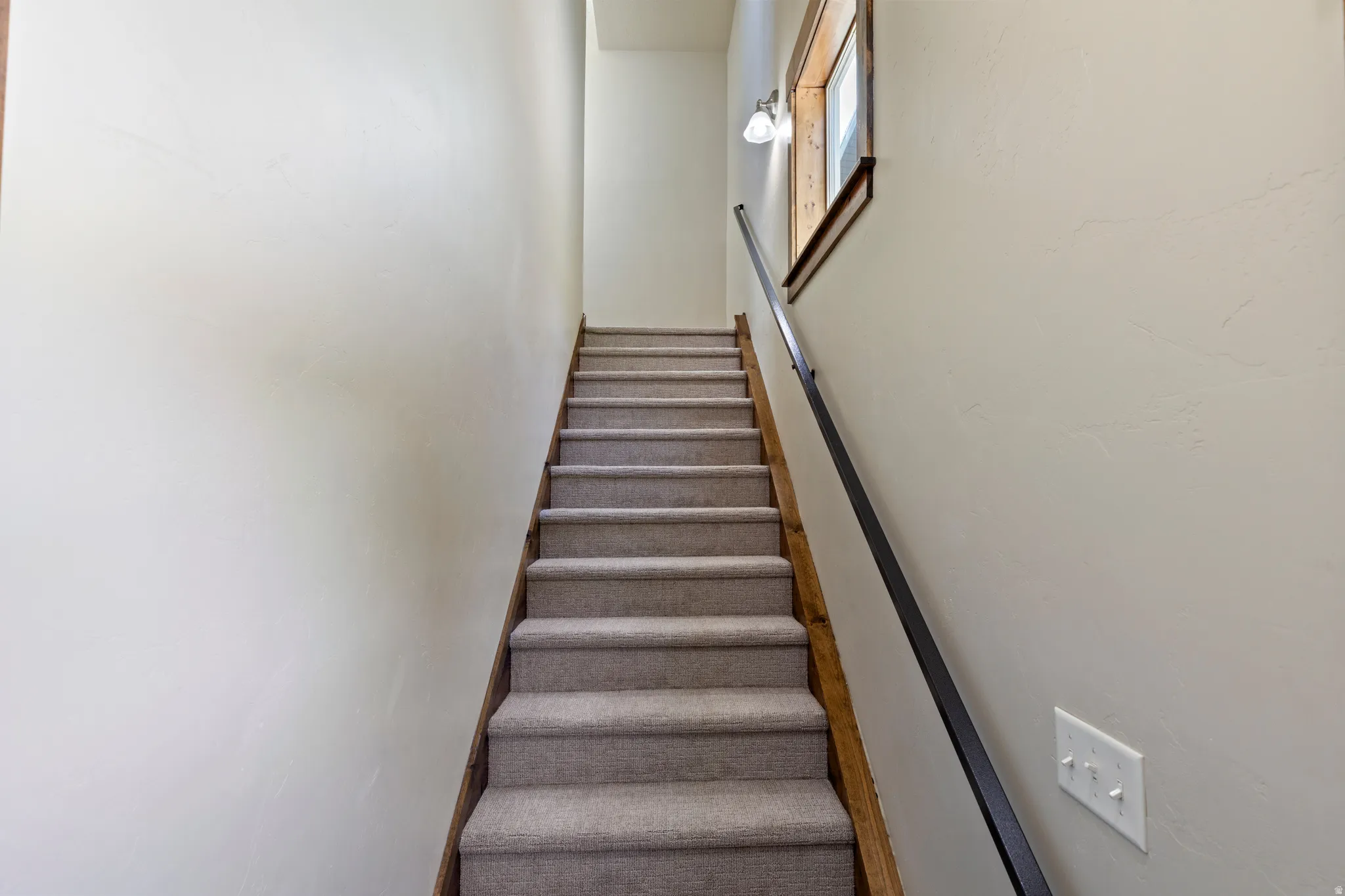 Carpeted staircase with a dark metal handrail and natural wood stringer