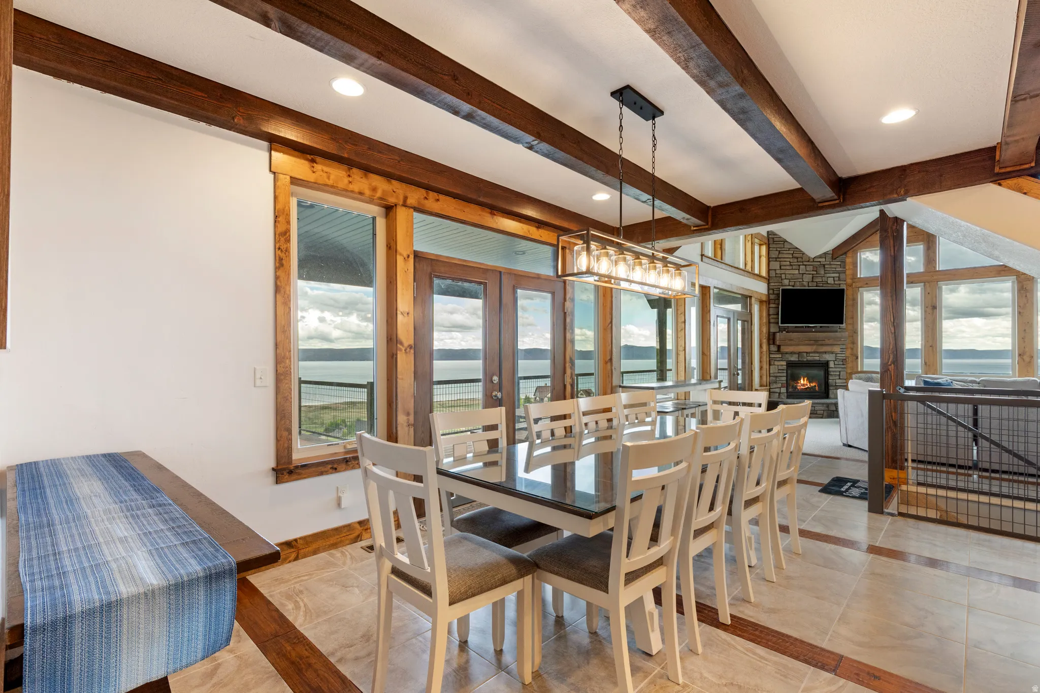 Spacious dining area featuring exposed wood ceiling beams, recessed lighting, and large windows with water scenery