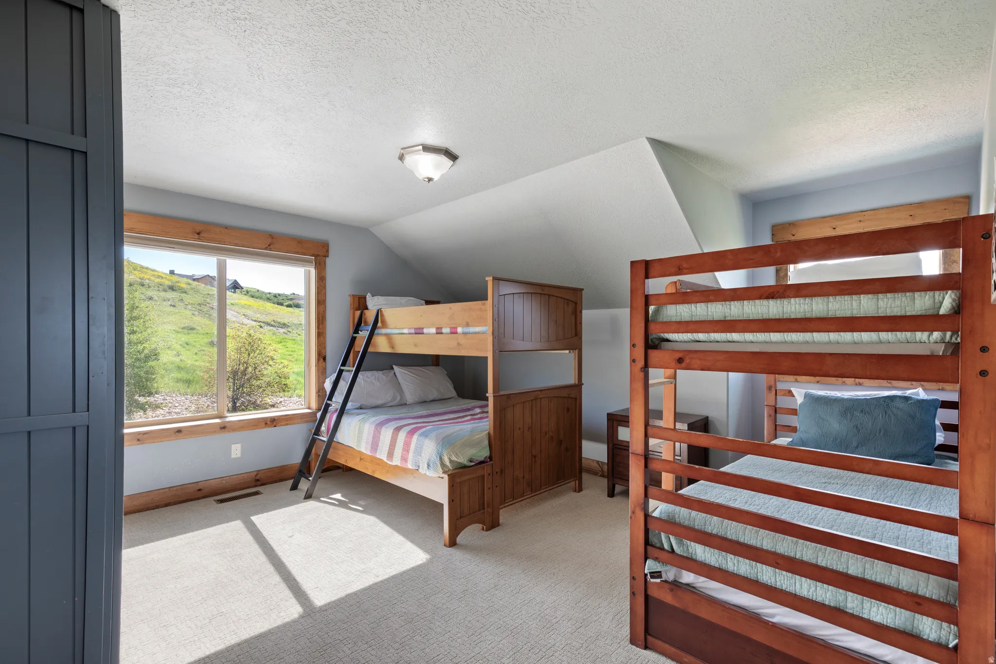 Carpeted room with a large window featuring natural wood trim, sloped ceiling, and a flush mount ceiling light