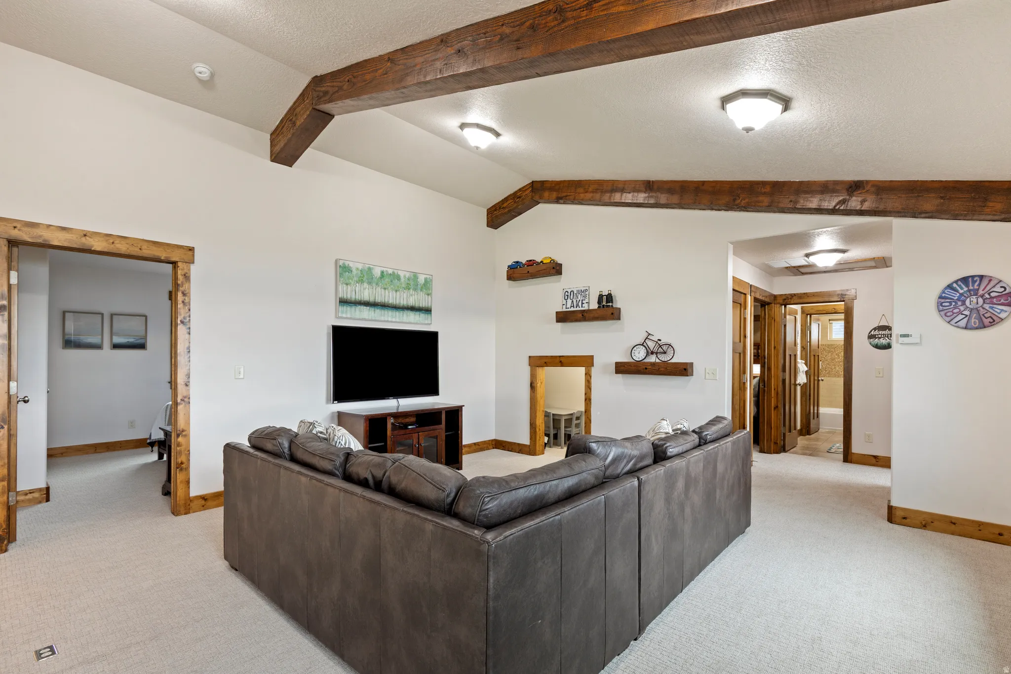 Spacious room featuring vaulted ceilings with exposed wood beams, light-toned carpeting, and natural wood trim around doorways
