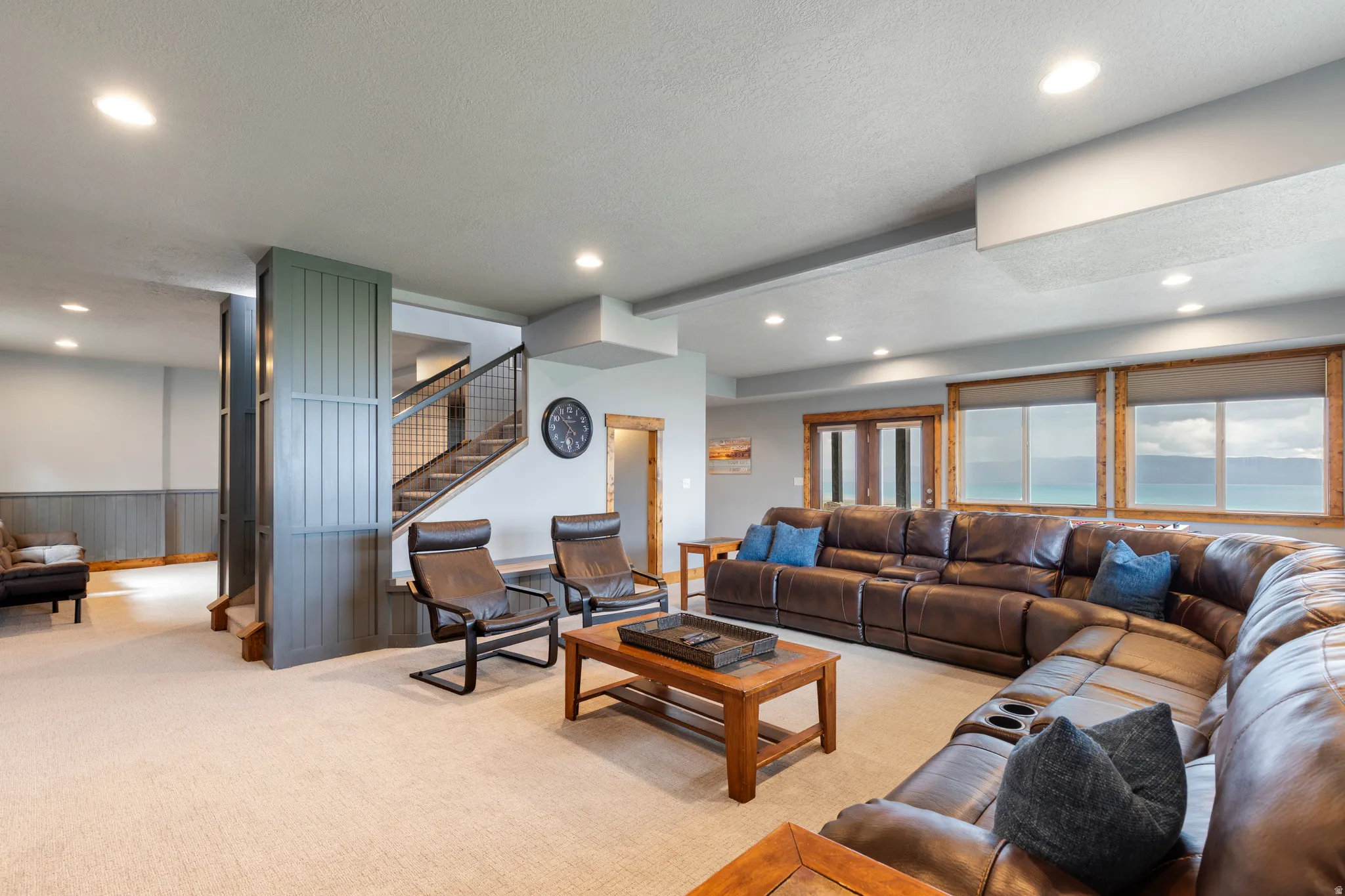 Spacious lower level living area featuring light-toned carpeting, recessed lighting, and a prominent wood staircase with black metal railings