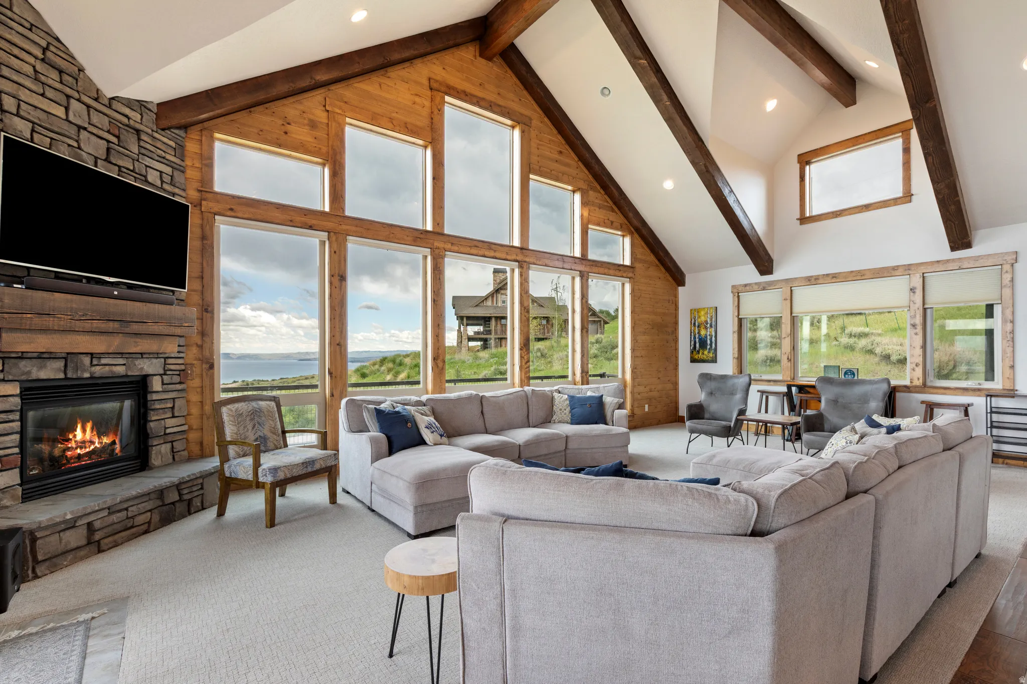 Vaulted living room featuring a stone fireplace, wood-finish accent wall, exposed wood beams, large picture windows, and recessed lighting