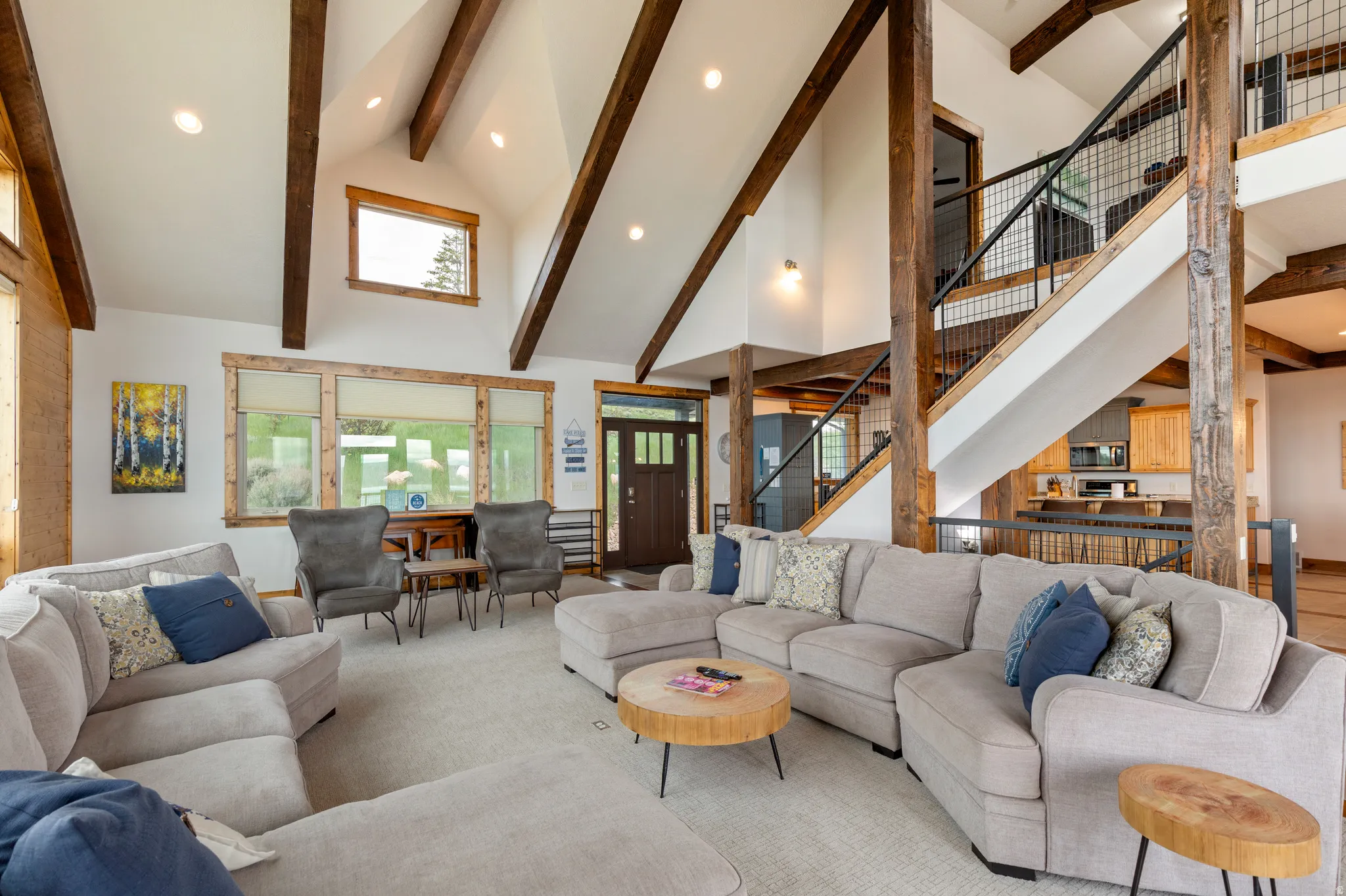 Living area featuring a vaulted ceiling with exposed wood beams, recessed lighting, and a prominent staircase with black metal railings