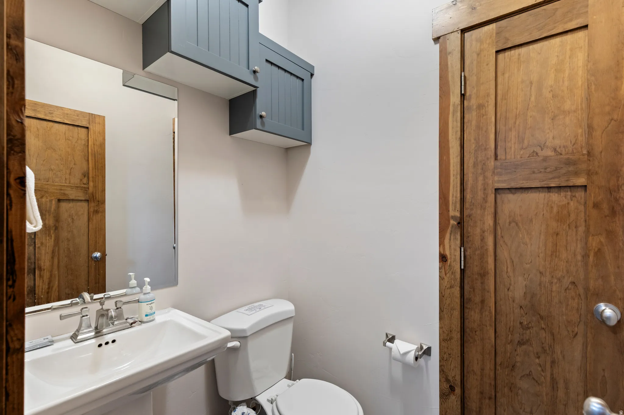 Pedestal sink with chrome-finish faucet, wall-mounted mirror, and complementary overhead cabinetry