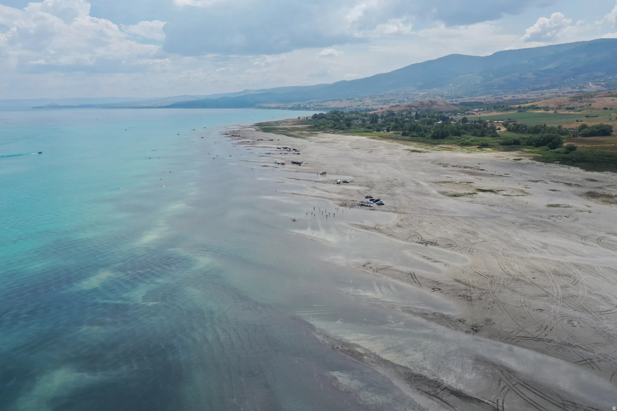 Expansive waterfront property featuring a wide sandy beach, clear turquoise waters, and distant mountainous terrain