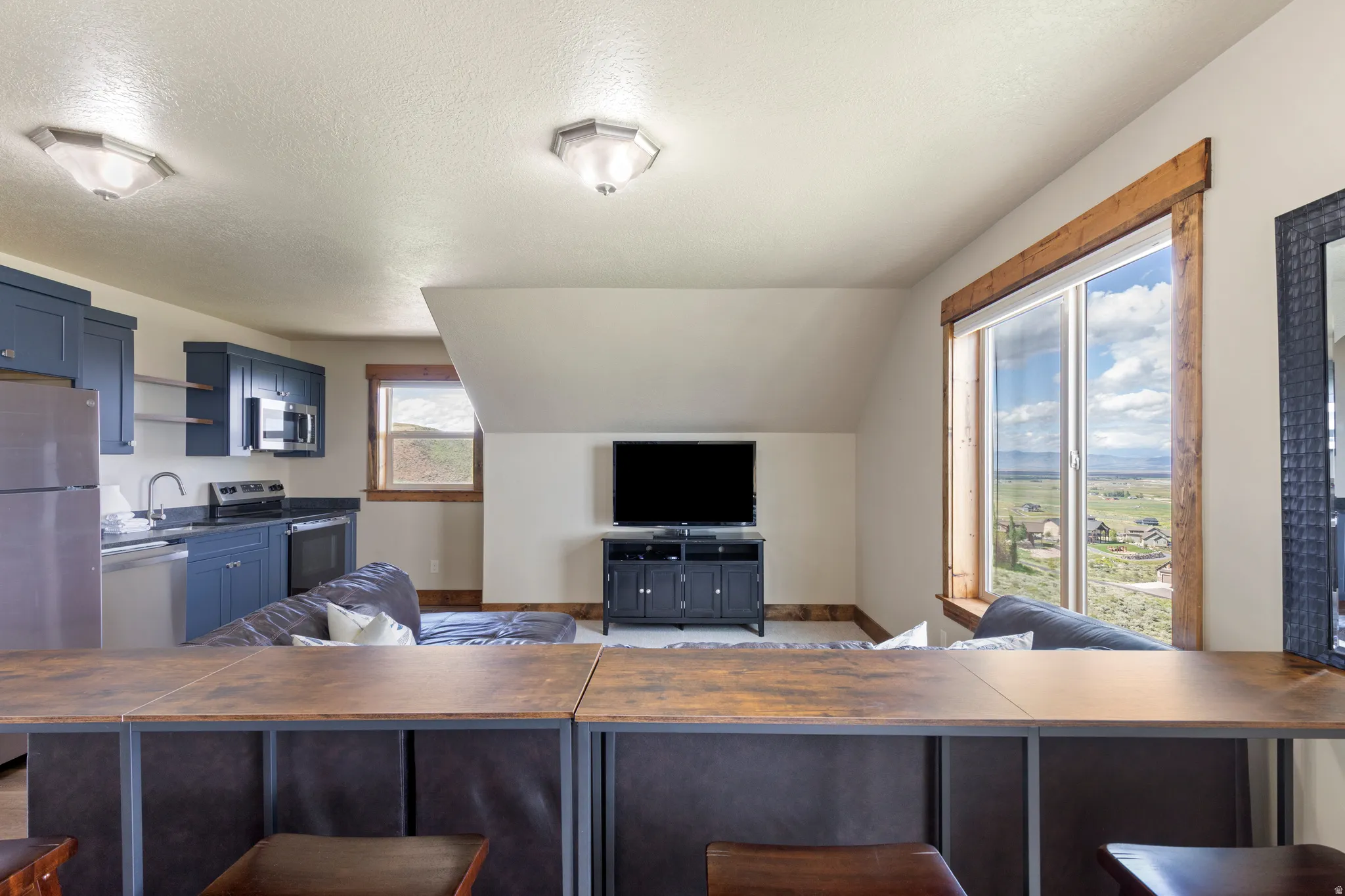 Open-concept living space with a full kitchen featuring blue cabinetry, stainless steel appliances, and a dark countertop