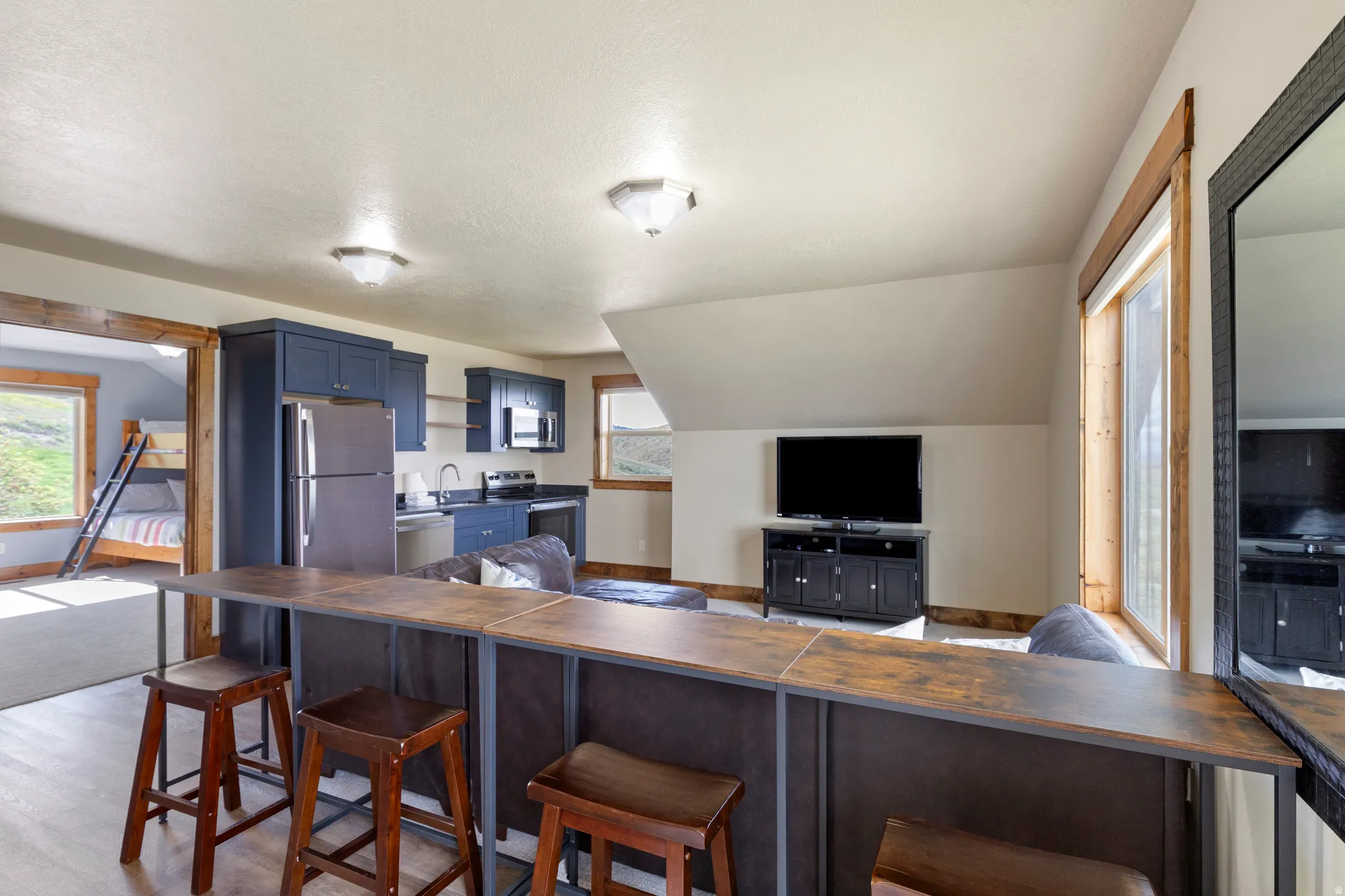 Open-concept living space featuring a breakfast bar with seating, a full kitchen with stainless steel appliances and blue cabinetry, and wood-finish flooring