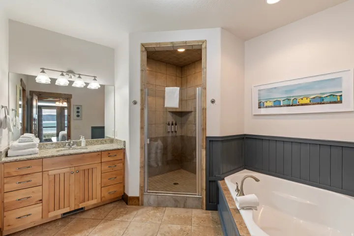 Bathroom featuring a built-in soaking tub, a stand-up shower with glass enclosure, a vanity with a light wood-finish cabinet and stone countertop, tile flooring, and wainscoting
