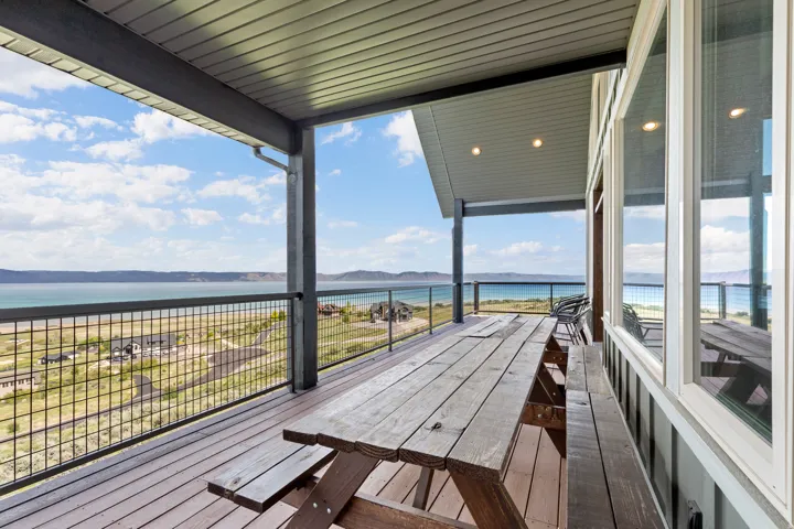 Expansive covered deck featuring composite decking, recessed lighting, white framed windows, and metal grid railing