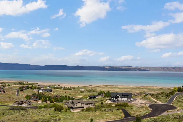 Expansive lakefront property featuring a sandy beach, clear blue water, and distant mountain ranges