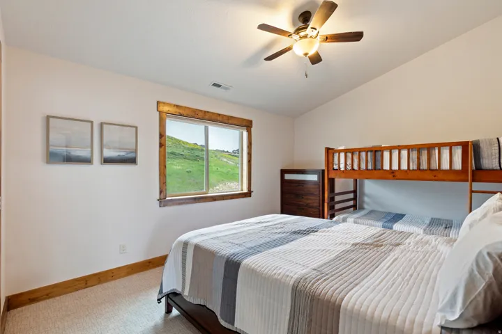 Bedroom with a large window featuring wood trim, textured carpeting, and a ceiling fan with integrated lighting