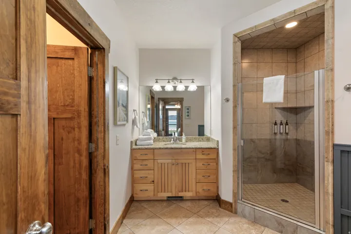 Spacious bathroom featuring a glass-enclosed shower with tile surround, a wood vanity with a stone-finish countertop, and decorative wall-mounted lighting