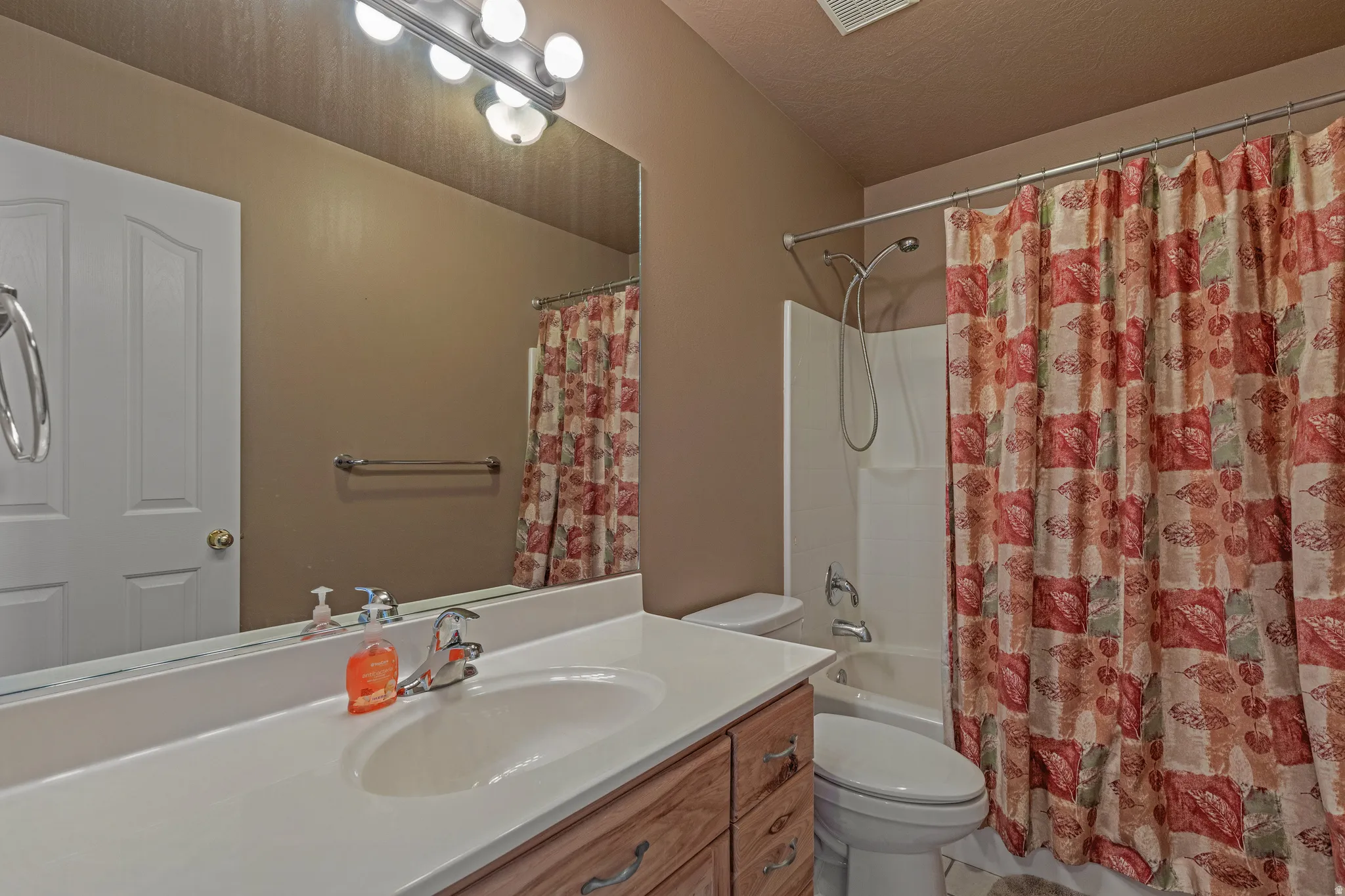 Bathroom featuring a wood-finish vanity with a white countertop and integrated sink, a large mirror, and a wall-mounted light fixture