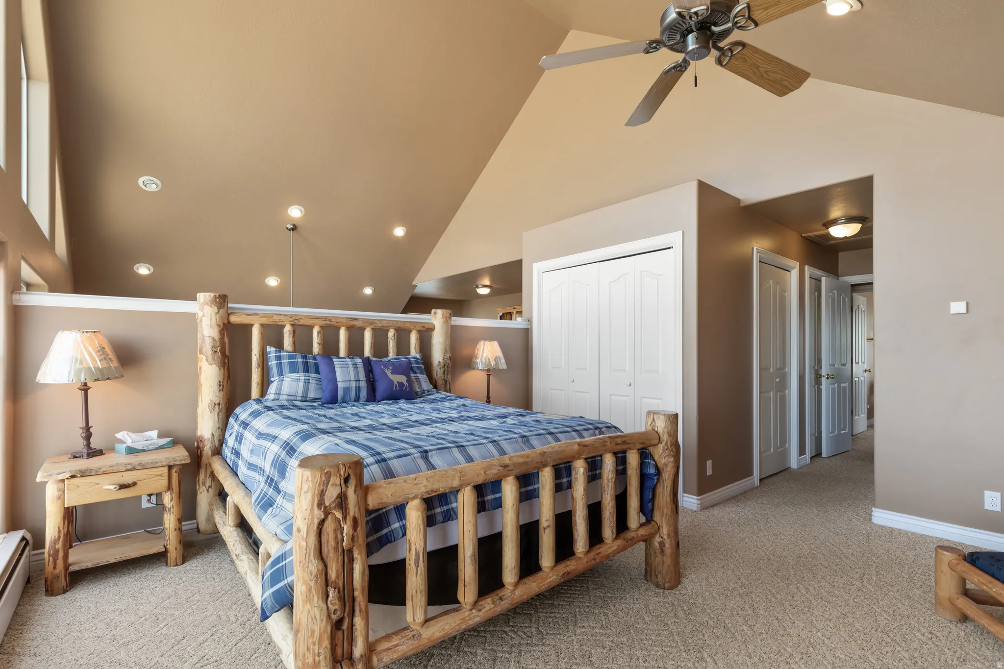 Carpeted room with a vaulted ceiling and exposed beams, featuring a wood-frame bed and coordinating nightstand