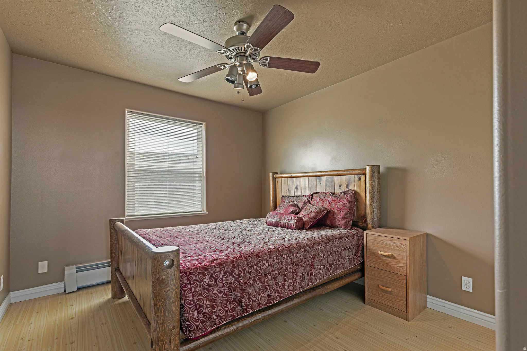 Bedroom featuring light wood-finish flooring, a window with horizontal blinds, and a ceiling fan with integrated lighting