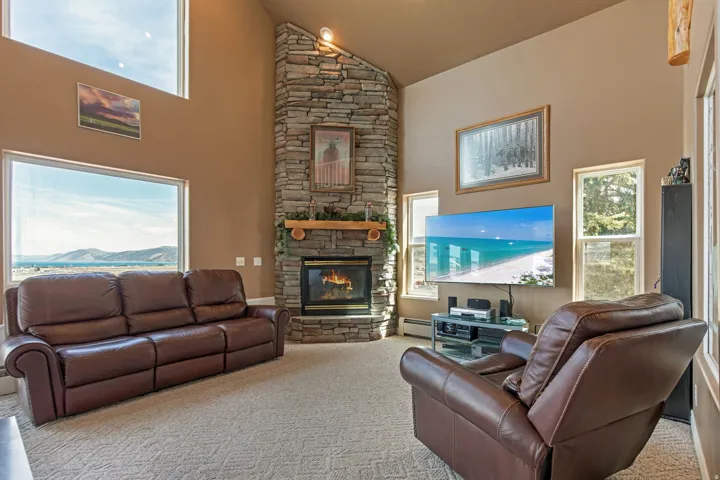 Living area featuring a stone fireplace with a wood mantel, vaulted ceilings, and large picture windows
