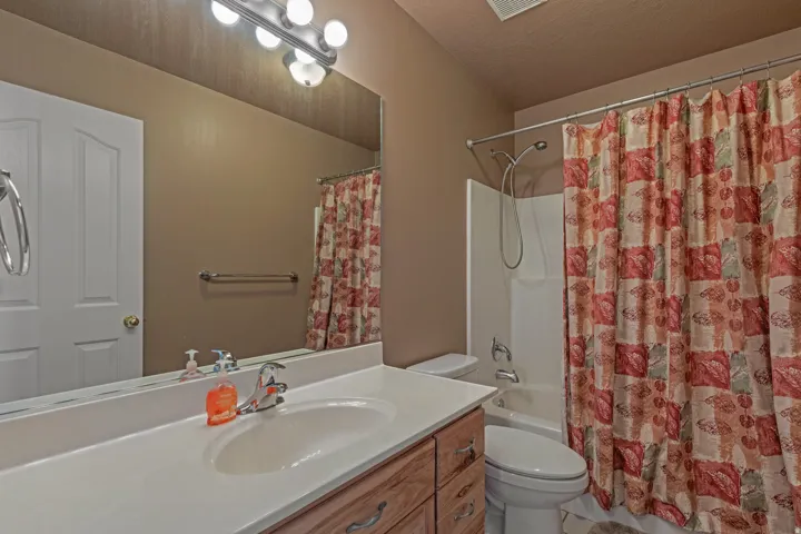 Bathroom featuring a wood-finish vanity with a white countertop and integrated sink, a large mirror, and a wall-mounted light fixture