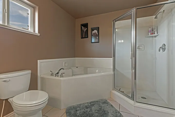 Bathroom featuring a corner soaking tub with chrome fixtures, a separate glass-enclosed shower, and a white toilet