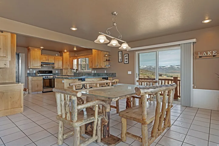 Open-concept kitchen and dining area featuring light wood cabinetry, stone countertops, stainless steel appliances, and tile flooring
