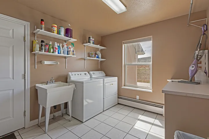 Utility room featuring white ceramic tile flooring, a utility sink, and wall-mounted shelving