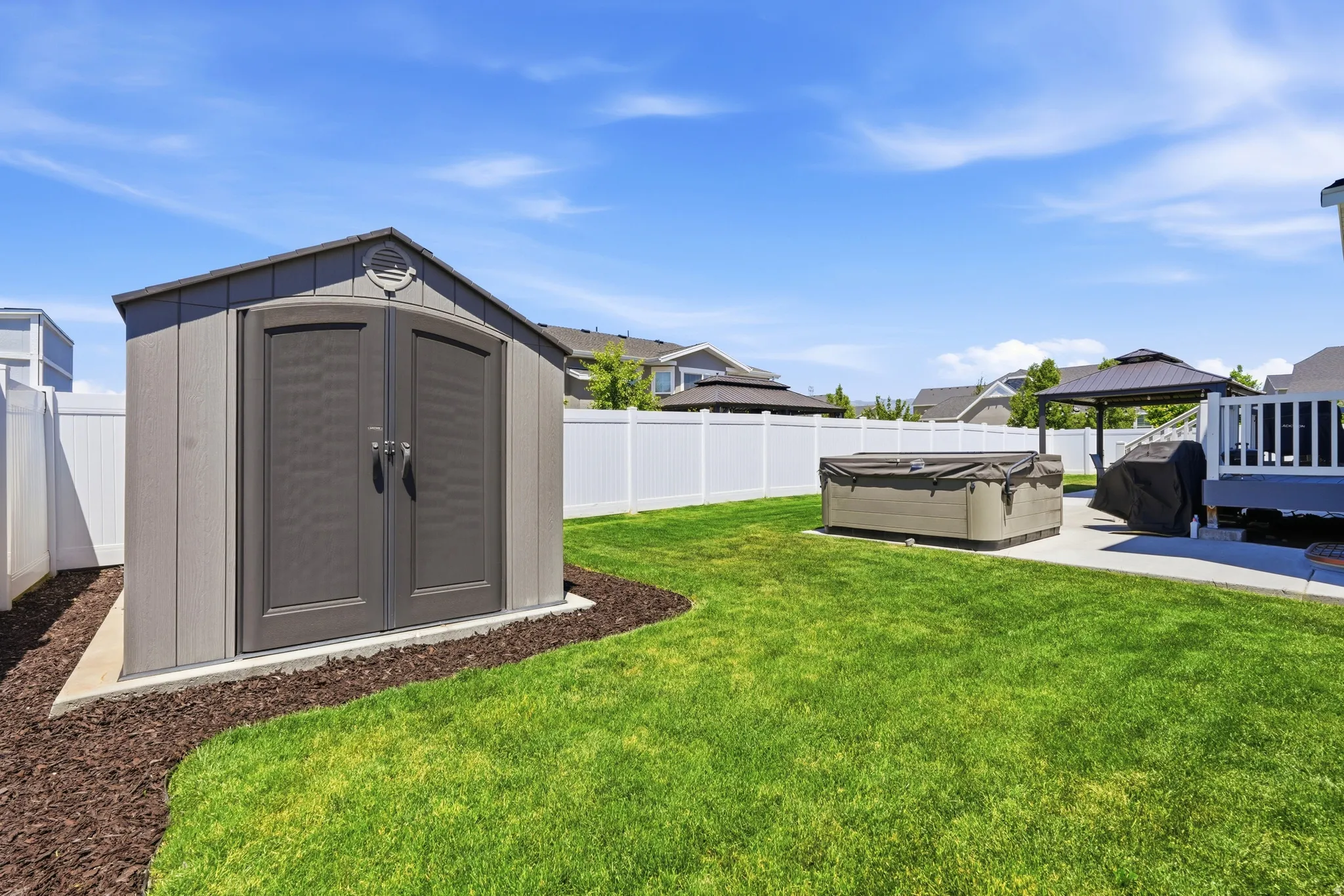 Spacious backyard featuring a white vinyl privacy fence, a storage shed, a paved patio, and a covered gazebo