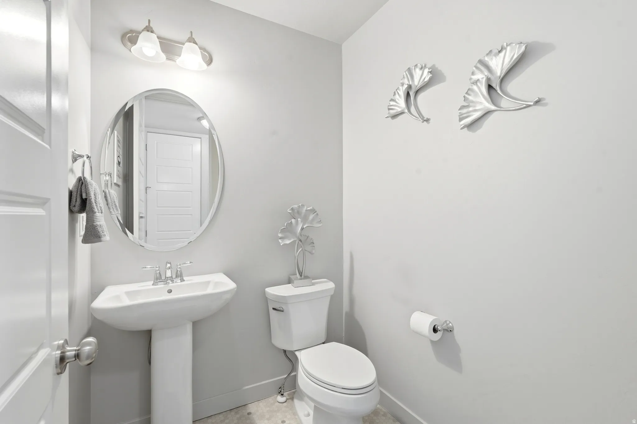 Half bathroom featuring a pedestal sink with chrome faucet, an oval mirror, and an overhead vanity light fixture