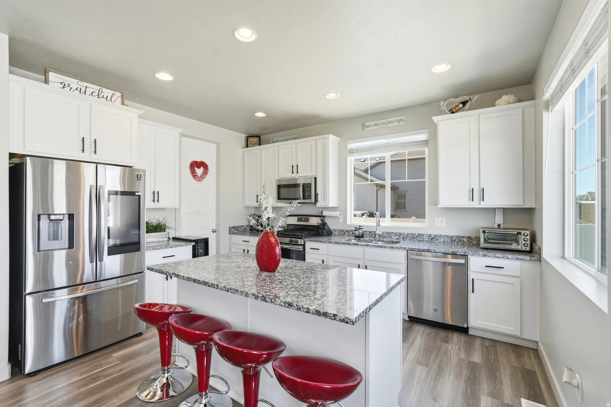 Bright kitchen featuring white cabinetry, granite-style countertops, stainless steel appliances, a central island, and wood-finish flooring