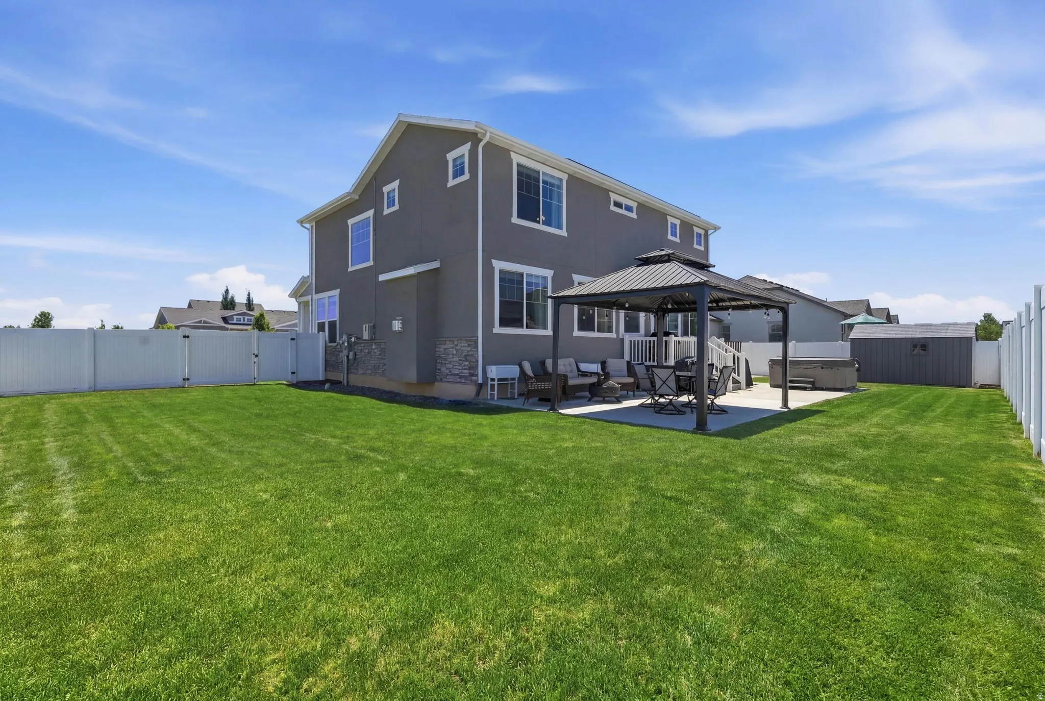 Expansive backyard featuring a large green lawn, concrete patio, and white vinyl perimeter fencing