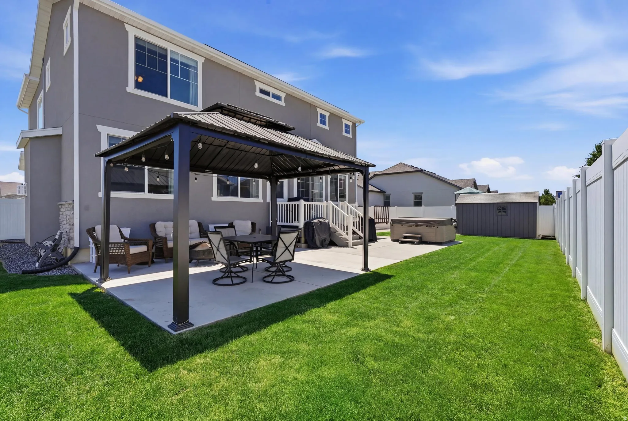 Expansive backyard featuring a large concrete patio with a gazebo, a manicured lawn, and a privacy fence