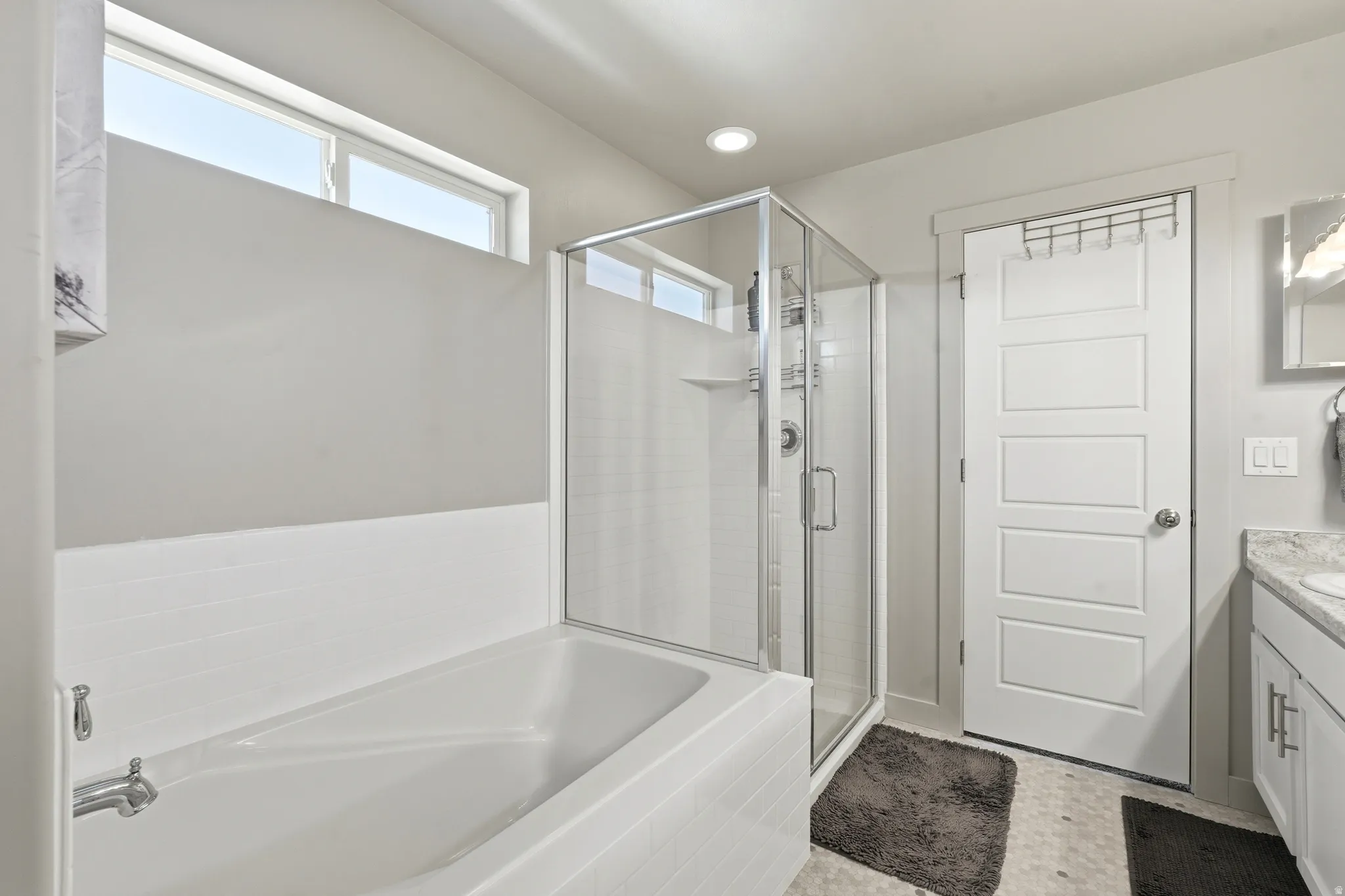 Bathroom featuring a white soaking tub, glass-enclosed shower, transom window, and a paneled door